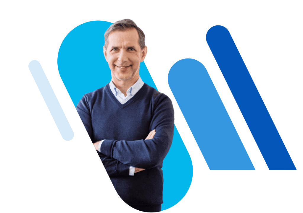 Mann mit verschränkten Armen, der ein hellblaues Hemd und darüber einen dukelblauen Pullover trägt und lächelt